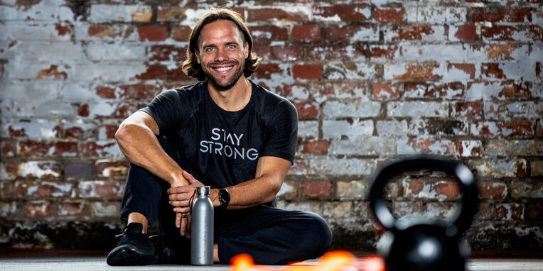 Timo Gudrich auf dem Boden sitzend mit einer Trinkflasche vor einer Steinwand