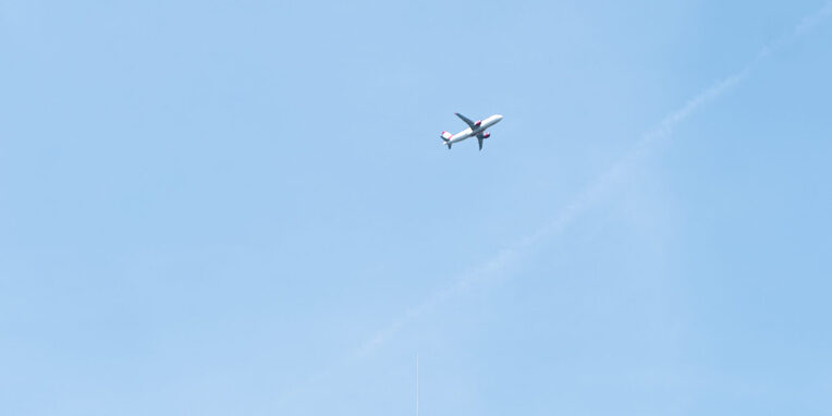 Blick auf das Außengebäude des Rathauses mit Uhr am Gebäude und Flugzeug am Himmel