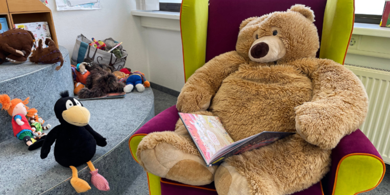 Teddybär sitzt im Sessel mit Buch auf dem Schoß