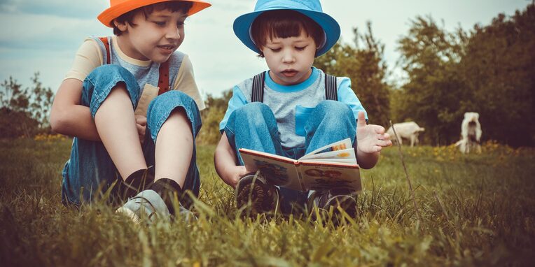 Kinder lesen im Gras sitzend ein Buch
