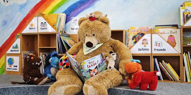 Teddybär umringt von Stofftieren liest aus einem Buch vor