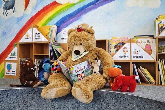 Teddybär umringt von Stofftieren liest aus einem Buch vor