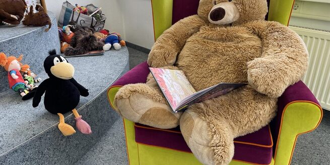 Teddybär sitzt in Sessel und liest vor