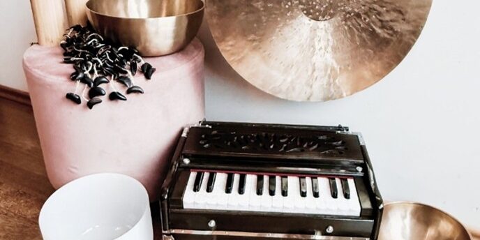 verschiedene Klangschalen, ein Gong,  ein kleines Minipiaano präsentieren sich auf einem braunen Holzboden