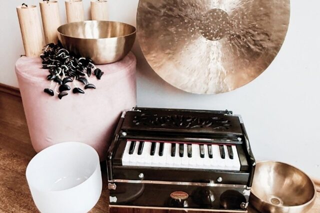 verschiedene Klangschalen, ein Gong,  ein kleines Minipiaano präsentieren sich auf einem braunen Holzboden