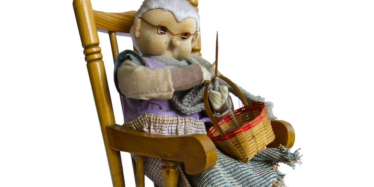 Eine Großmutter in Puppenfigur strickend auf einem Schaukelstuhl sitzend
