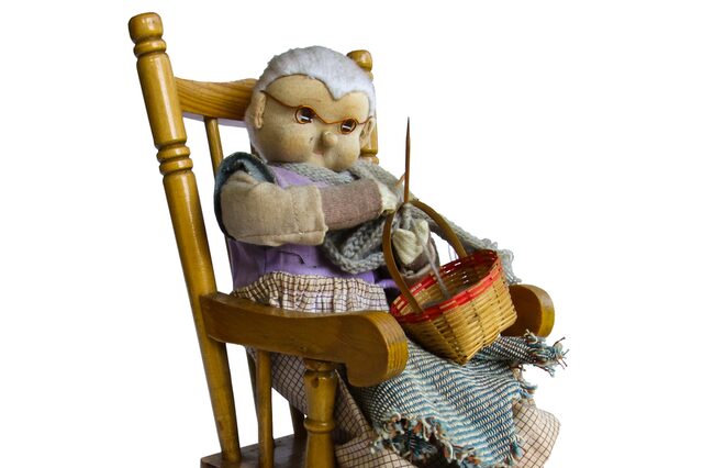 Eine Großmutter in Puppenfigur strickend auf einem Schaukelstuhl sitzend