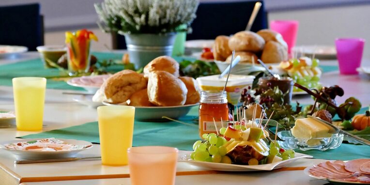Gedeckter Frühstückstisch mit Brötchen, Wurst, Marmelade, Käse, Trauben