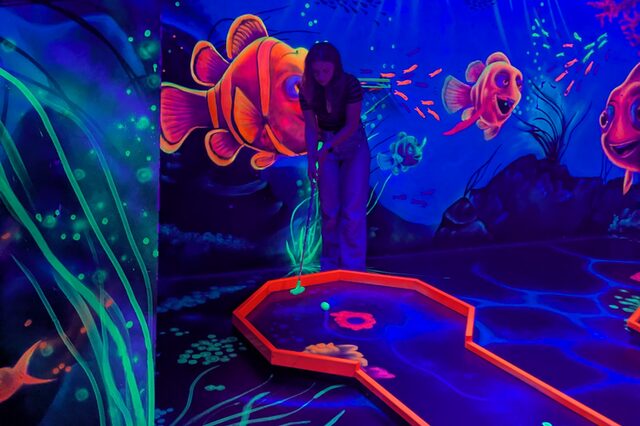Ein blauses Bild mit einer rotumrandeten Minigolfbahn und angedeuteten Pflanzen und roten Fischen in einem Aquarium