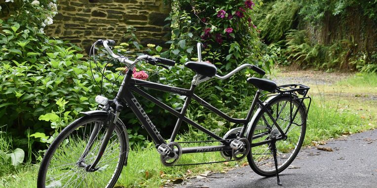 Ein schwarzes Tandem-Fahrrad auf einem Waldweg vor einer Steinmauer
