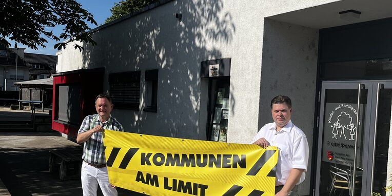 Vlnr: Bürgermeister Dirk Gene Hagelstein und Erster Stadtrat Stefan Schmitt vor dem Familienzentrum Gartenstraße mit dem gelben Banner "Kommunen am Limit"