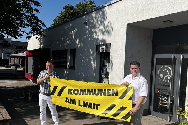 Vlnr: Bürgermeister Dirk Gene Hagelstein und Erster Stadtrat Stefan Schmitt vor dem Familienzentrum Gartenstraße mit dem gelben Banner "Kommunen am Limit"