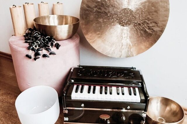 verschiedene Klangschalen, ein Gong,  ein kleines Minipiaano präsentieren sich auf einem braunen Holzboden