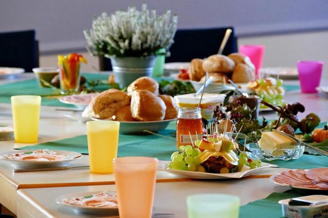 Ein gedeckter, farbenfroher Frühstückstisch mit Brötchen, Butter, Marmelade und Obstvariationen