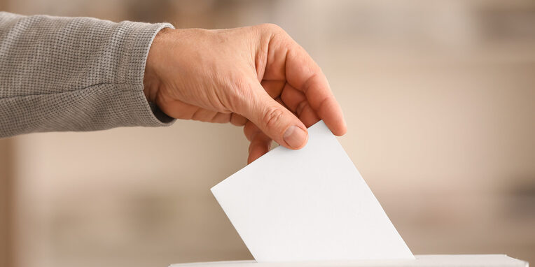 Hand, die Stimmzettel in eine Box wirft