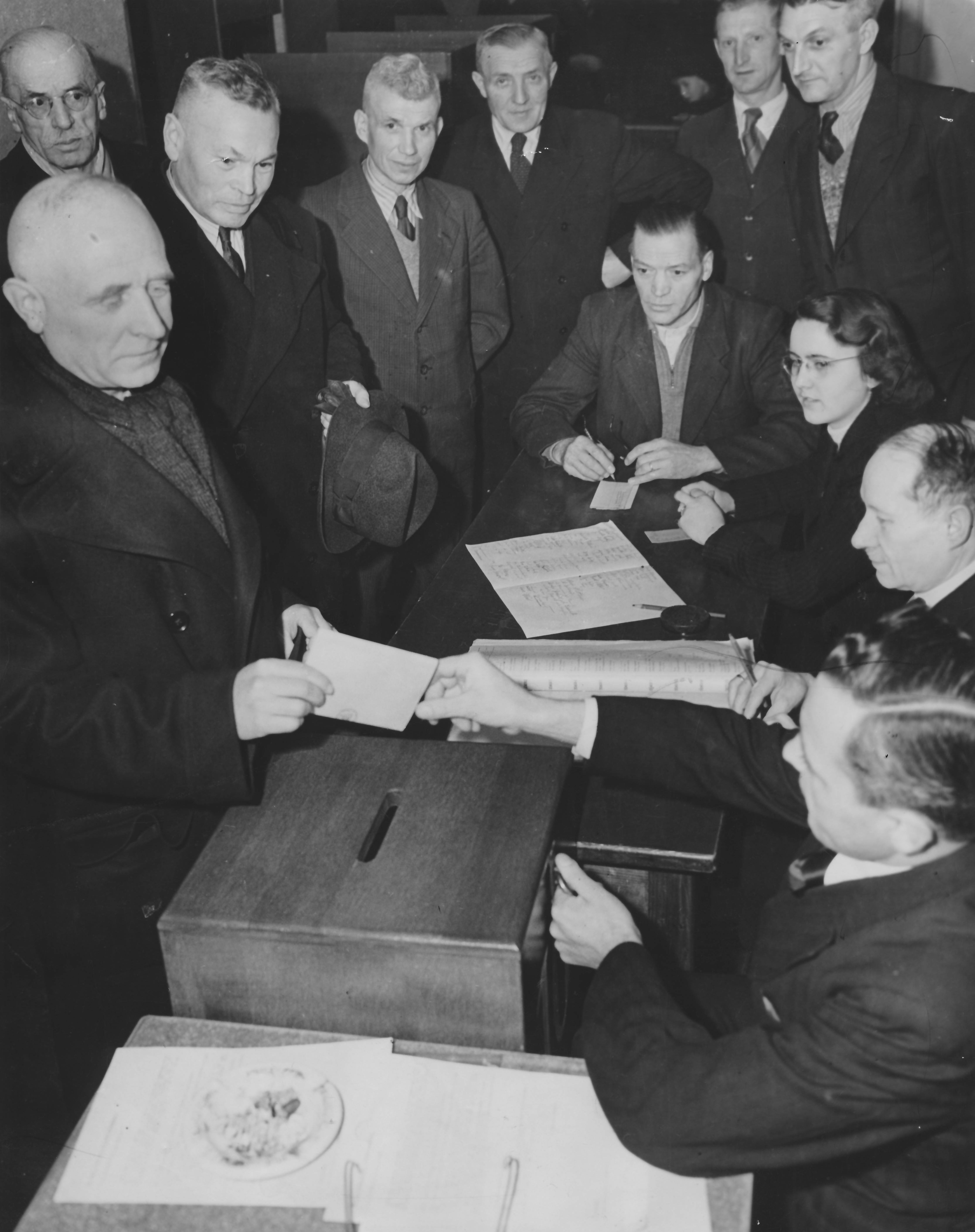 Das Bild zeigt die Stimmabgabe des Bürgermeisters Wilhelm Arnoul bei der Gemeinderatswahl am 27. Januar 1946 im Wahllokal in der Westendhalle. Zu sehen sind daneben v.l.n.r.: Georg Koser, Adolf Bauer, Philipp Wiemer, Adam Ebner, August Geiß (sitzend), Dr. Juliane Girardi-Vogt, Heinrich Zimbrich, Unbekannt, Fotograf: Paul Zehner, Offenbach]. Quelle: Stadtarchiv NI F 2.3 Nr. 49 Bld. 1