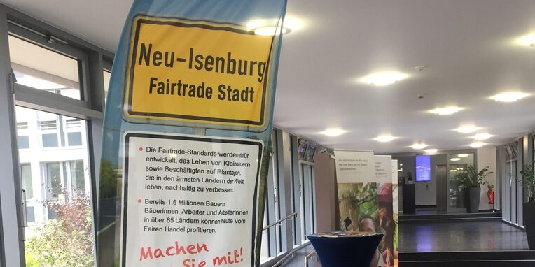 Fahne mit "Neu-Isenburg Fairtrade Stadt" steht im Foyer des Rathauses